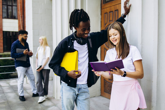 Smiling young students from diverse backgrounds collaborating and learning together with books on a university campus