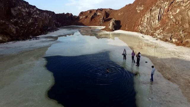 Aerial view of visitors exploring a frozen salt dome lake with someone swimming in a deep dark hole, highlighting the unique tourist experience within this epic geological landscape view.