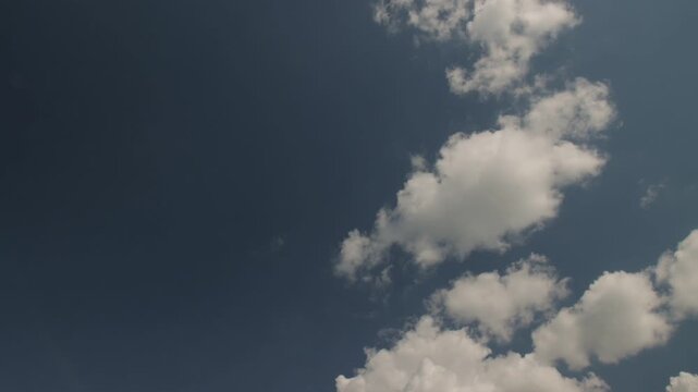 Time-lapse of large white cumulus cloud breaking apart and dispersing into small wispy clouds across deep blue sky