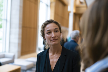 Fototapeta premium A well-dressed woman engages in conversation with a colleague in a bright, modern interior, highlighting professional interactions in contemporary workspaces.