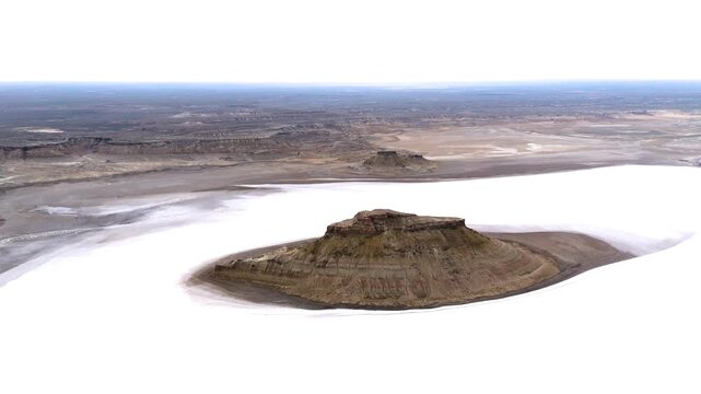 A cinematic side drone shot highlighting a massive rocky outlier in the foreground with a second cliff formation in the distance, set within the misty, water-covered salt flat  Karynzharyk Kazakhstan