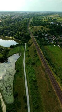 Vertical drone footage capturing railway tracks extending through the countryside during daytime. Aerial view highlighting transportation infrastructure and the surrounding landscape.