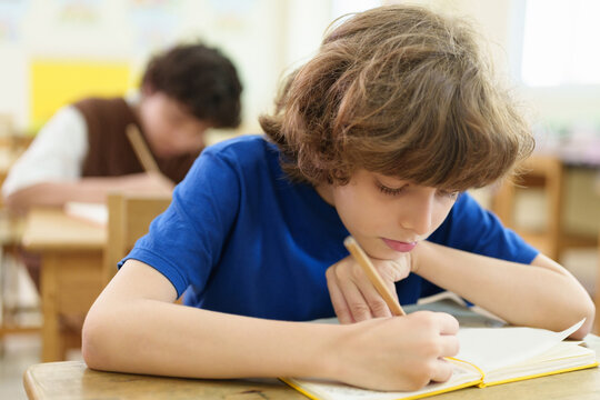 Focused elementary school boy writes carefully during a classroom exam, reflecting concentration, academic assessment, and independent learning.