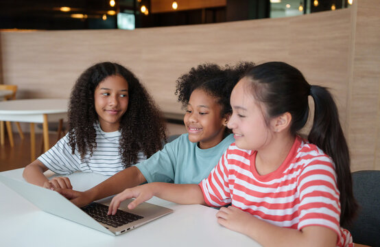 Diverse primary school children collaborate around a laptop, sharing ideas and learning together in a modern classroom, highlighting teamwork and digital education.