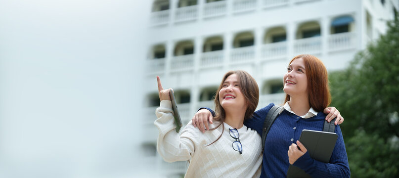 Two university friends enjoy time together on campus while holding digital tablets, expressing friendship, student lifestyle, collaboration, and modern education outdoors.