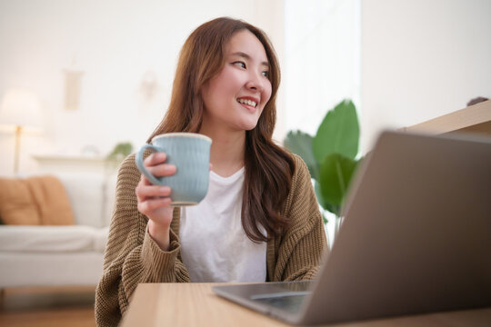Young woman enjoys a coffee break while studying online with a laptop at home, balancing digital learning, relaxation, and productivity in a comfortable modern workspace.
