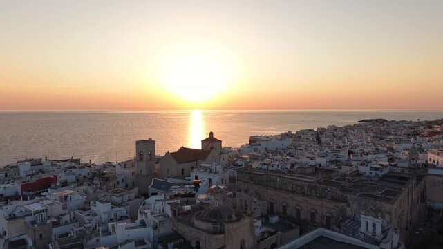 Scenic aerial view of polignano a mare's old town and cathedral with the sun rising over the calm adriatic sea, creating a beautiful and peaceful golden reflection