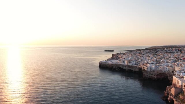 Golden hour sunrise over the stunning coastal town of polignano a mare in puglia, italy, featuring whitewashed houses perched on cliffs above the adriatic sea