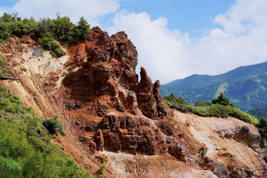 夏の日差しを浴びる赤褐色の岩肌が特徴的な地獄谷の断崖と、青空と緑豊かな山々が織りなす大自然のダイナミックな景観。