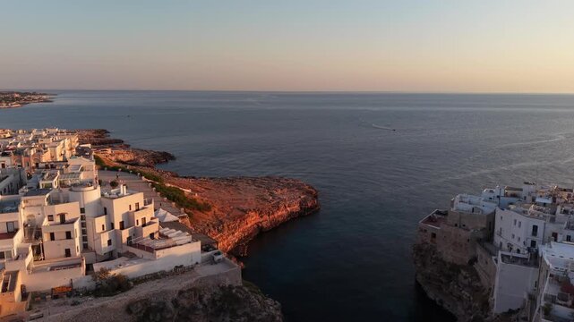 Scenic aerial view showing the charming coastal town of polignano a mare in puglia, italy, featuring whitewashed buildings perched on cliffs above the calm adriatic sea at sunrise