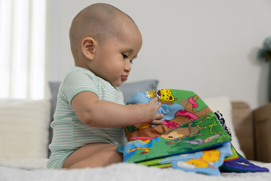 Baby book reading infant toddler bed bedroom home learning colorful cloth book held by curious bald child in striped bodysuit during quiet early education play
