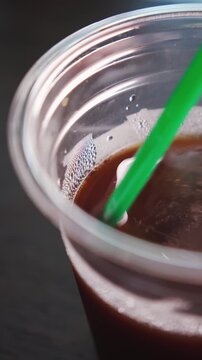Close-Up of Stirring Iced Coffee in a Single-Use Plastic Cup with Plastic Straw