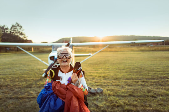Smiling senior skydiver with parachute at sunset airfield