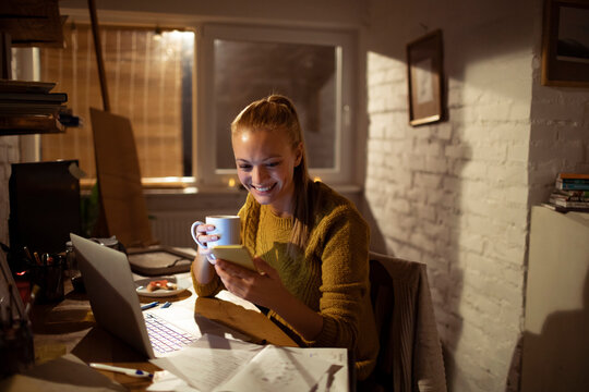 Smiling woman using smartphone and laptop at home office at night