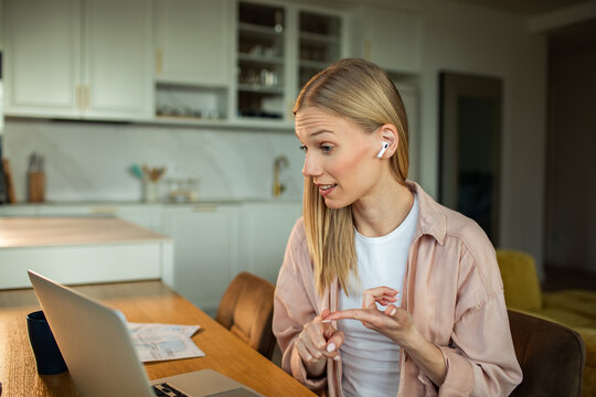 Young woman with earbuds on video call at home kitchen
