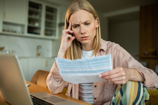Worried young woman reading bill at home kitchen table