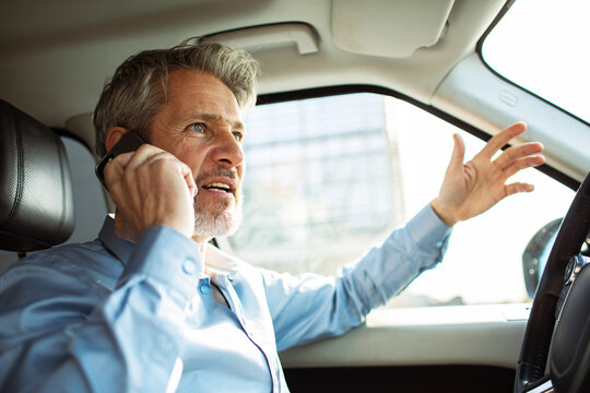 Mature man talking on smartphone while driving car