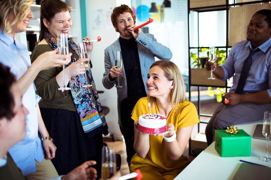Coworkers celebrating a birthday with cake in a modern office