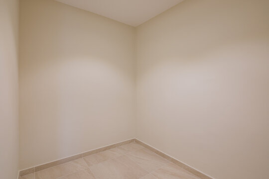 Empty beige interior room with tiled floor, soft natural light, clean neutral walls, unfurnished layout, minimalist style, calm residential space for modern property use