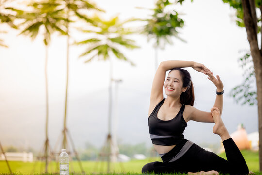 Young Asian woman practicing yoga outdoors in green park at sunrise