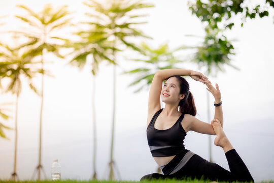 Young Asian woman practicing yoga outdoors in green park at sunrise