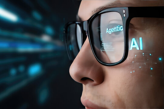 A close-up profile photo of a person wearing black-rimmed glasses, with a digital holographic interface projected onto the lenses and face. The interface displays the text 'Agentic' and 'AI' in glowin