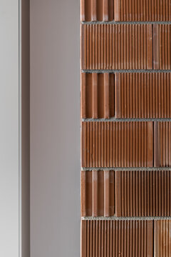 Textured brown ribbed brick wall with warm earthy tones, close architectural surface detail, vertical pattern, subtle relief, and contemporary building finish for decorative facade
