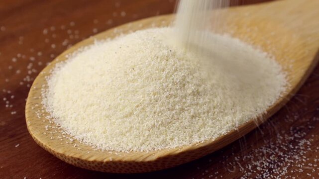 Semolina falling down into the wooden spoon close up