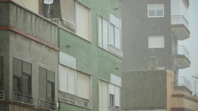 Facades of southern houses with roller shutters on windows during rain. Overcast day with heavy rainfall. Streaks and dampness on exterior walls of houses.