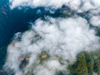 Aerial view of thick white clouds drifting over the green forest peaks of Sanqingshan Mountain in Jiangxi province of China during a bright sunny day © AS_SleepingPanda