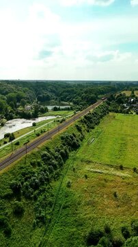 Vertical drone footage capturing railway tracks extending through the countryside during daytime. Aerial view highlighting transportation infrastructure and the surrounding landscape.
