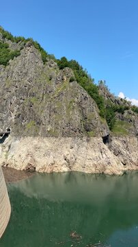Vertical shot of a slow pan over Vidraru Dam and Lake with clear green water reflections in Fagaras Mountains along Transfagarasan road, Romania. Impressive hydroelectric arch dam landscape.