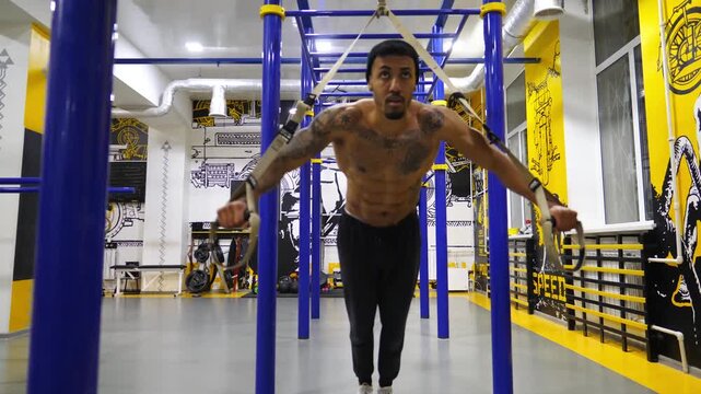 Young afro american sportsman doing exercises on trx equipment at sport club. Muscular african athlete hard training at modern gym. Strong black man working out at fitness centre. Sportive lifestyle
