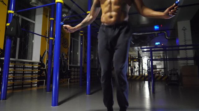 Male feet of athlete skipping with a jump rope at sport club. Legs of young sportsman exercising at fitness centre. Sporty man in sportswear doing cardio at modern gym. Concept of active lifestyle