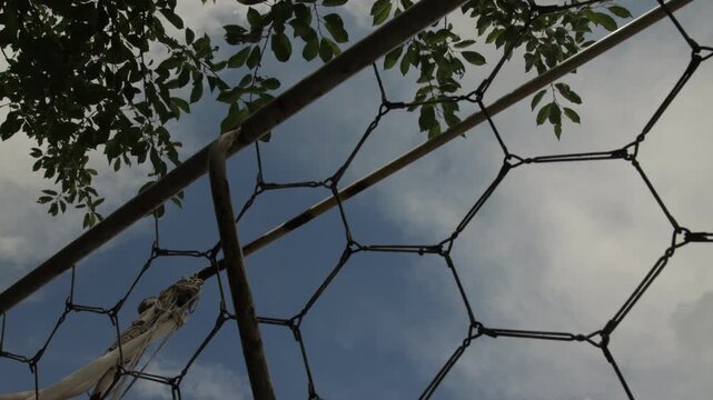 Old metal outdoor swing frame beneath leafy tree branches and cloudy blue sky