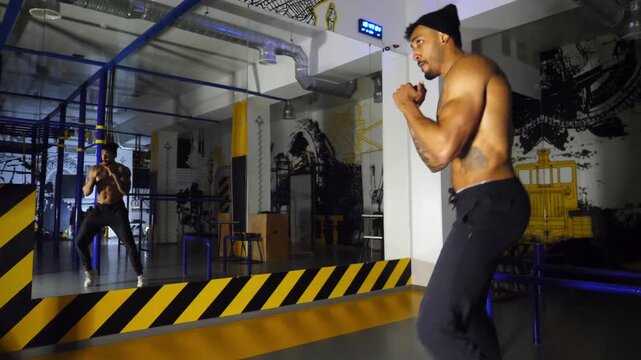 Young afro american sportsman practicing shadow boxing at modern gym. Muscular african boxer demonstrating punches the air indoor. Strong black kickboxer training at fitness centre. Healthy lifestyle