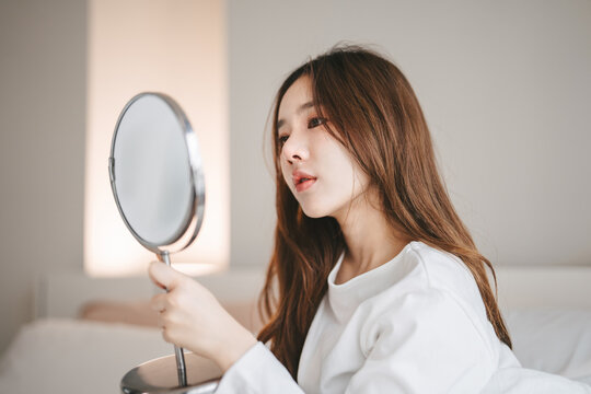 Beauty skin young asian woman looking mirror checking acne wrinkles on her face for skin care routine