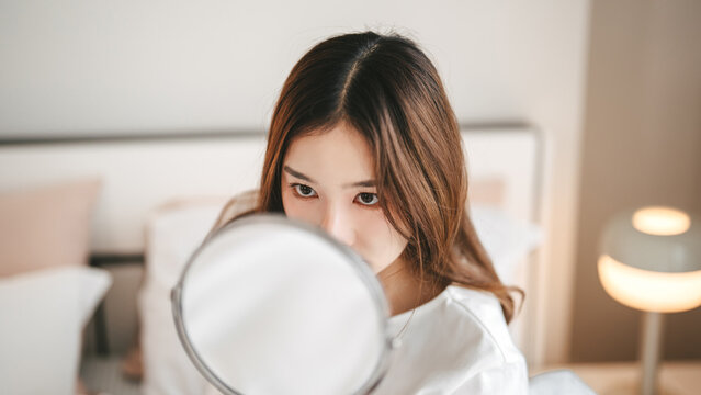 Beauty skin young asian woman looking mirror checking acne wrinkles on her face for skin care routine