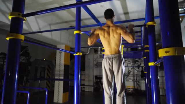Muscular sportsman doing pull ups on horizontal bar at modern gym. Strong male athlete working out at sport club. Young sportsperson exercising at fitness centre. Concept of healthy active lifestyle