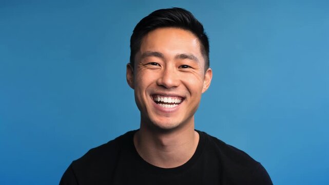 Happy young Asian man smiling with bright teeth wearing black shirt on blue background