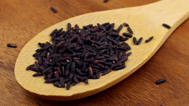 Black or Purple Rice or Riceberry falling down into the wooden spoon close up
