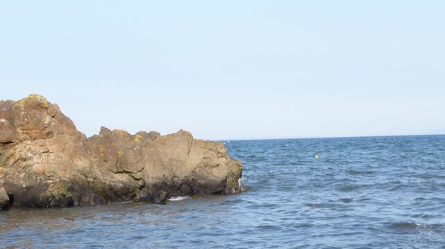 Scenic view of a calm blue sea gently lapping against a rugged rock formation on a clear day