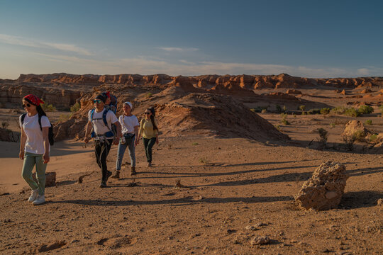 Front view of group of young friends with child in backpack carrier hiking in desert canyon. Active family tourists exploring remote scenic rocky valley wilderness at sunset.