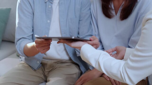 Asian couple signing digital contract on tablet screen during meeting, happy husband and wife signing electronic signature on tablet, clients approving digital insurance contract or investment.