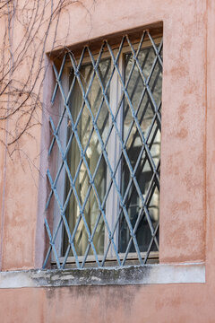 Window with diamond-pattern metal security bars on a residential facade, symbolizing home protection, burglary prevention, privacy, safety, and restricted access.