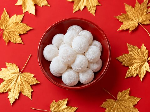 Delicate white coconut candies in a red bowl surrounded by golden maple leaves on a vibrant red background