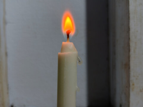 Burning white candle with bright orange flame and dripping wax closeup