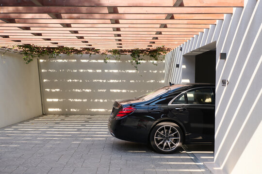 Luxury Black Sedan Parked in Modern Garage Under Wooden Pergola with Dramatic Shadows