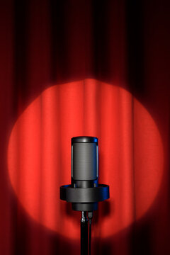Microphone on theater stage on red curtains illuminated by a spotlight.