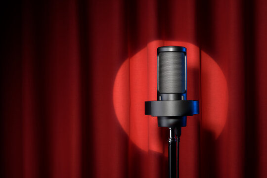 Microphone with spotlight on red stage curtain.